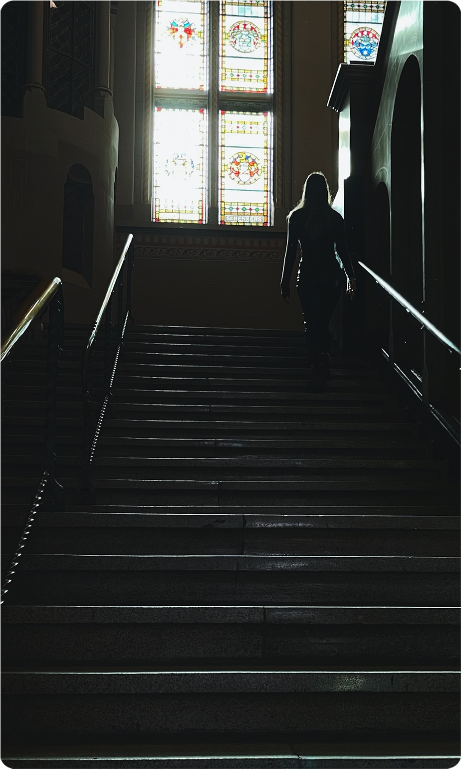 Silhouette of a person walking up stairs with stained glass windows