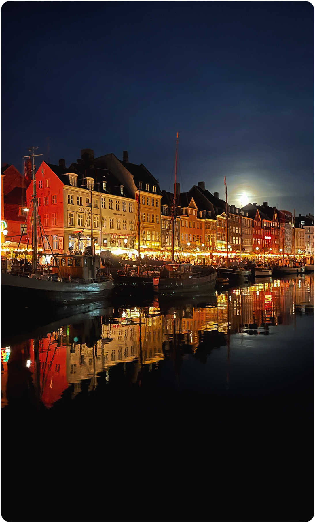 Colorful buildings along Copenhagen waterfront at night with reflections in water